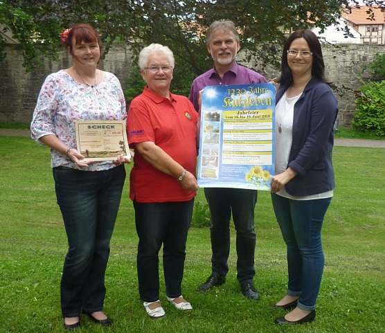 Doreen Deutsch vom Kindergarten, Hella Brand von den Landfrauen und Andrea Krausel vom Heimatverein freuen sich auf das Jubil&auml;um und pr&auml;sentieren stolz den Spendenscheck sowie das Veranstaltungsplakat. (Foto: Pressestelle Landratsamt Unstrut-Hainich Kreis)