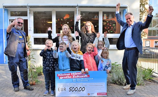 Die Vorsch&uuml;ler des Kindergartens Am Neuen Ufer in M&uuml;hlhausen sind die Th&uuml;ringer Sieger des Wettbewerbs Kleine H&auml;nde, gro&szlig;e Zukunft. Kreishandwerksmeister Roland Reichenbach (links) und der Pr&auml;sident der Handwerkskammer Erfurt, Stefan Lobenstein (rechts), &uuml;bergaben einen Scheck in H&ouml;he von 500 Euro und kleine Geschenke. (Foto: Susann Eberlein/HWK Erfurt)