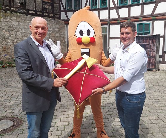 Markus Edom vom Kultur-Referat der Stadt M&uuml;hlhausen, Maskottchen Wurschti und der Betriebsleiter des Bratwurstmuseums, Kay Wipprecht, mit der Goldenen Axt, die bei den traditionellen Wettbewerben zur Holzfahrt am Samstag in mehreren Kategorien verliehen wird (Foto: Stadtverwaltung M&uuml;hlhausen)