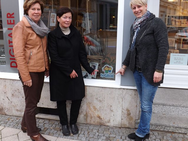 Bild: Katja Klaus, Regina Haupt und Birgit Schmidt (v. r.) pr&auml;sentieren das Notinsel-Logo im Schaufenster des Fotogesch&auml;fts am Frauentor in M&uuml;hlhausen. 